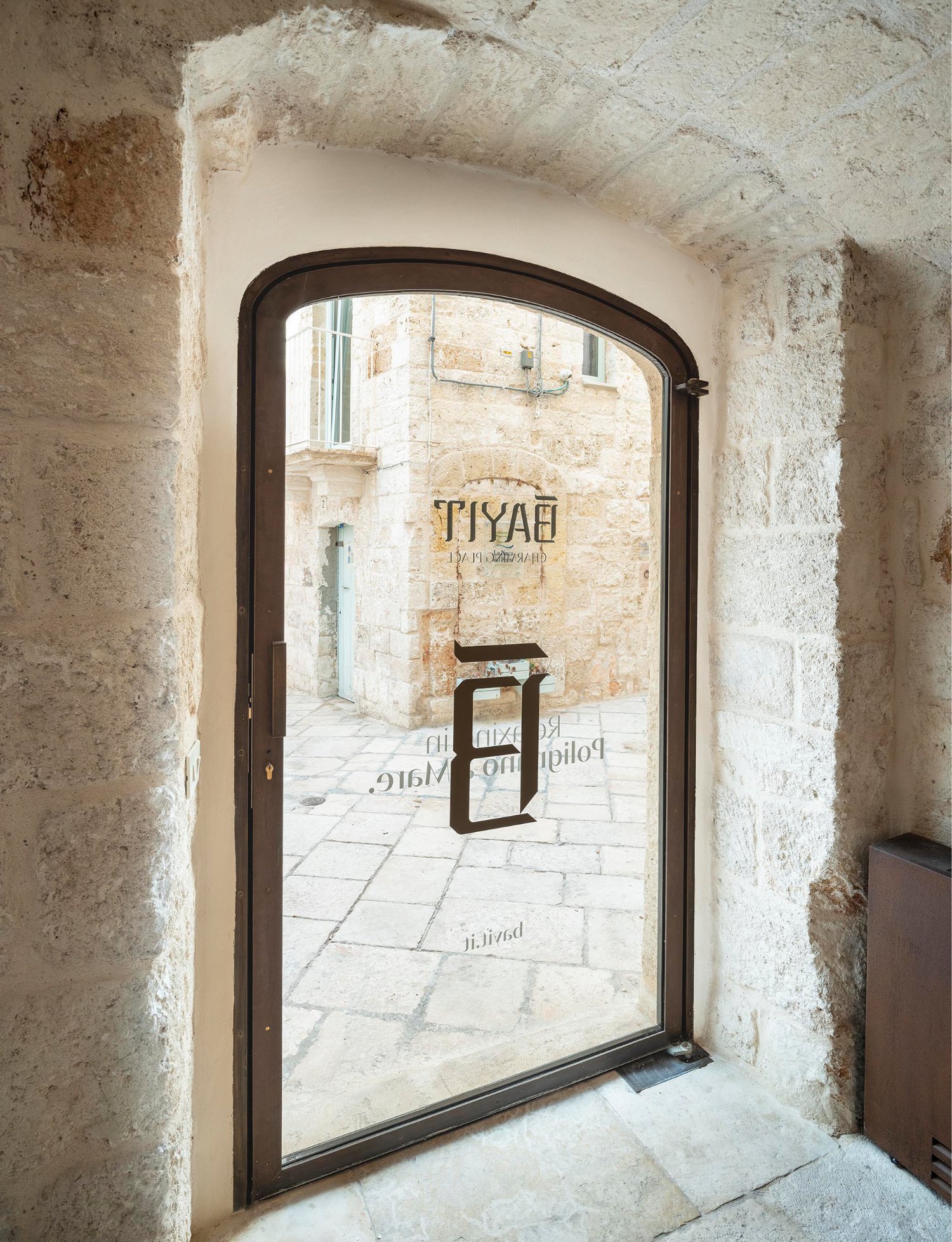 Arched bronze-framed glass door set into a whitewashed stone portal