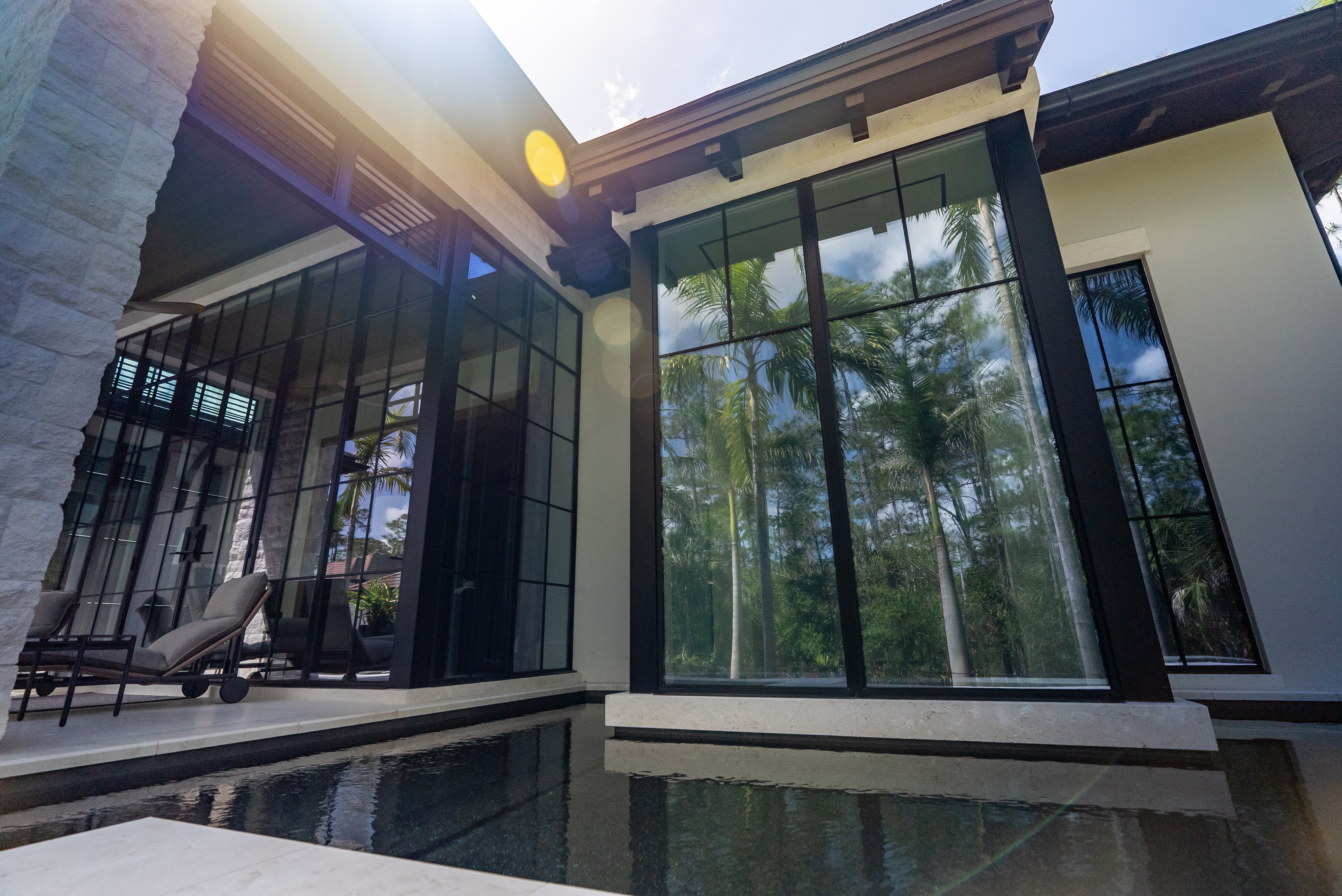 Floor-to-ceiling Milano steel window wall reflecting palms over a black-bottom reflecting pool